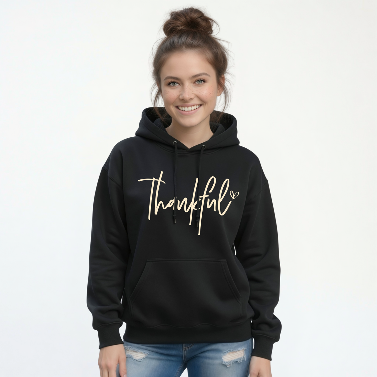 Woman wearing a black pullover hoodie with a gold Thankful script design and blue jeans