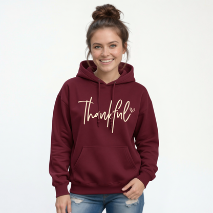 Woman modeling a maroon pullover hoodie with a white Thankful script design on a white background