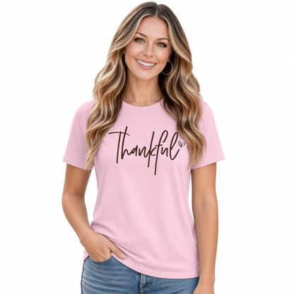 Woman modeling a light pink T-shirt with a white Thankful script design on a white background