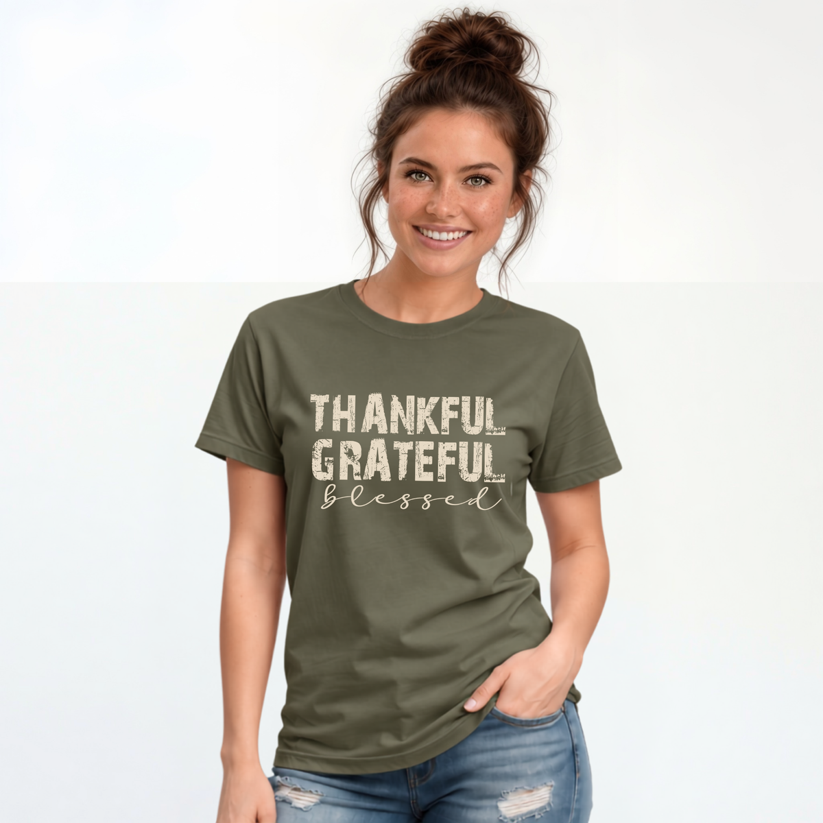 Woman wearing a military green T-shirt with distressed Thankful Grateful Blessed lettering on a plain white background.