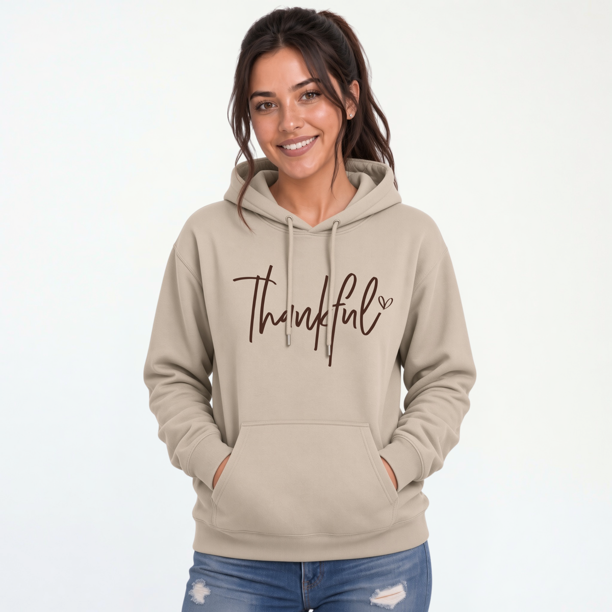 Woman wearing a sand pullover hoodie with a brown Thankful script design and blue jeans