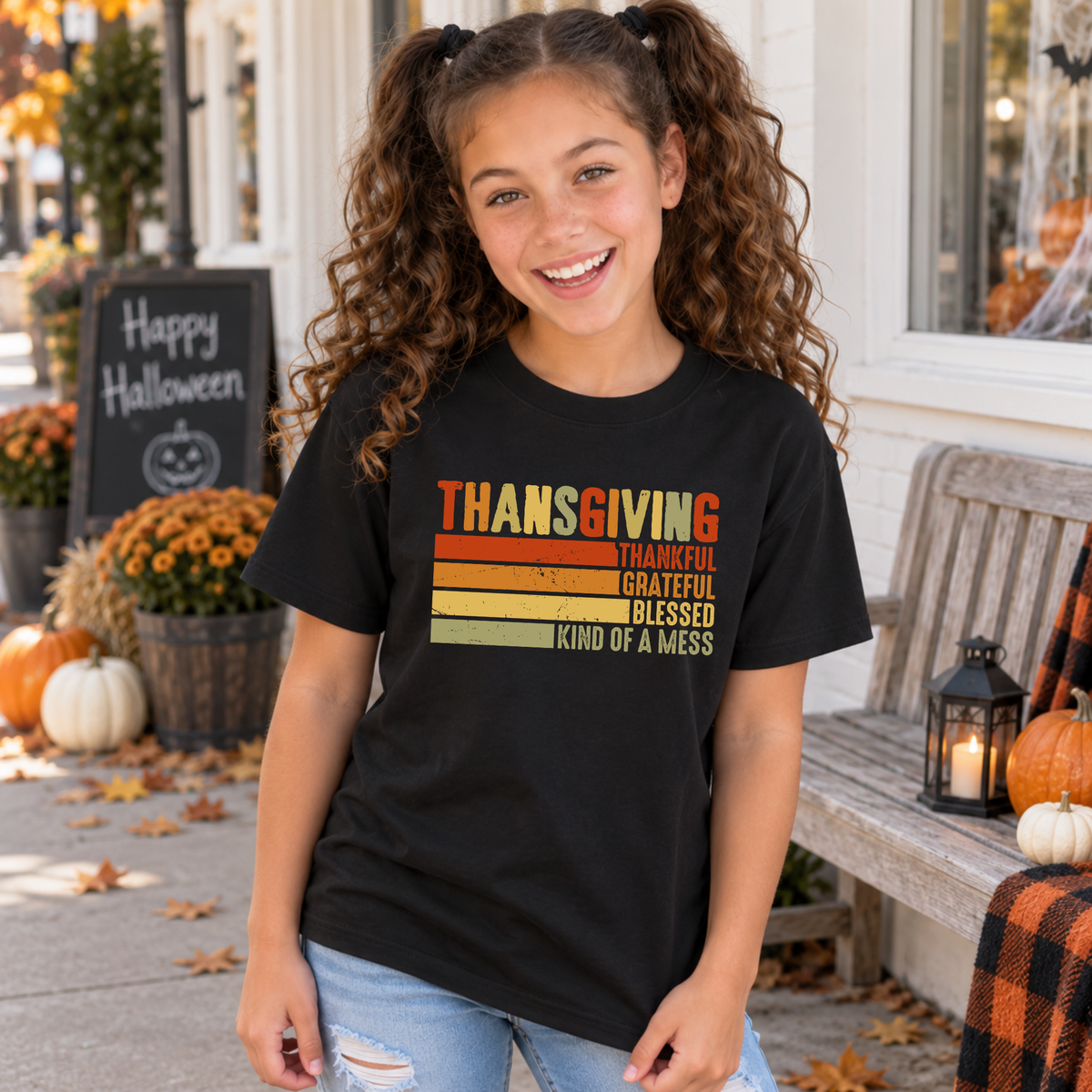 Girl wearing a black youth T-shirt with retro Thanksgiving Thankful Grateful Blessed Kind of a Mess design near pumpkins.