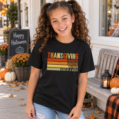 Girl wearing a black youth T-shirt with retro Thanksgiving Thankful Grateful Blessed Kind of a Mess design near pumpkins.
