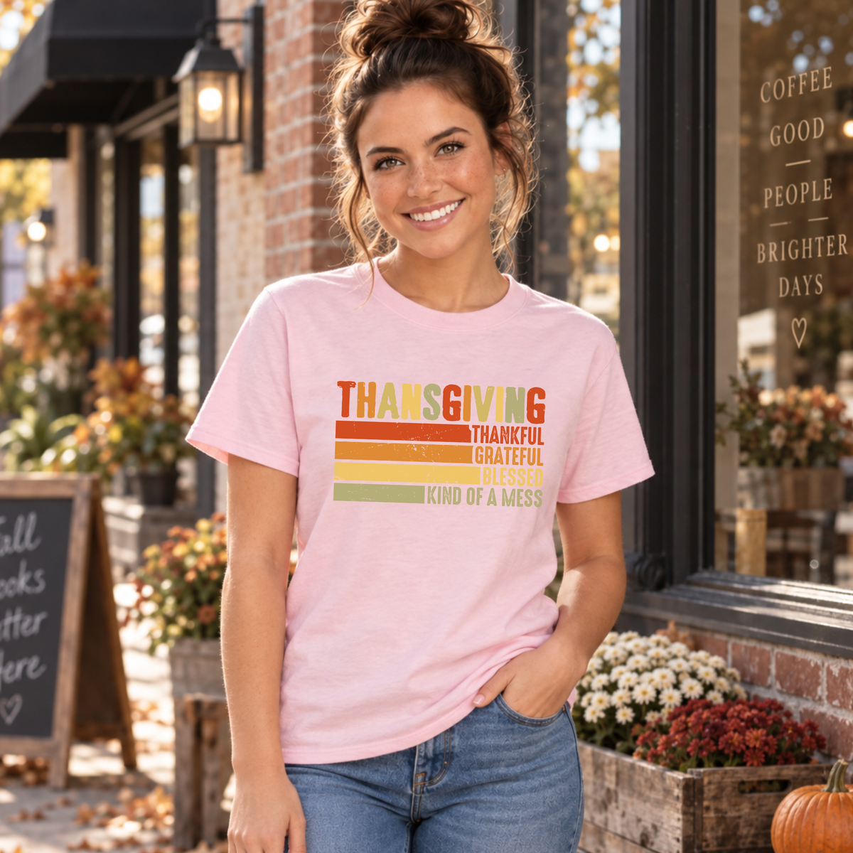 Woman wearing a light pink T-shirt with retro Thanksgiving Kind of a Mess design outside a fall cafe.
