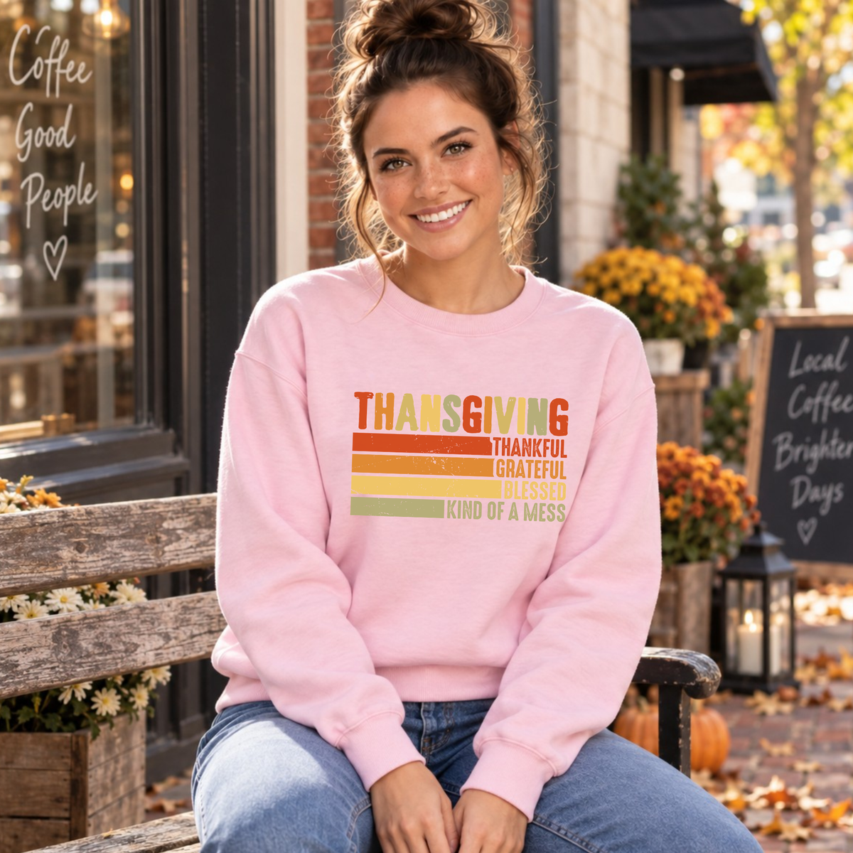 Woman seated in a light pink sweatshirt with retro Thanksgiving Thankful Grateful Blessed Kind of a Mess design.