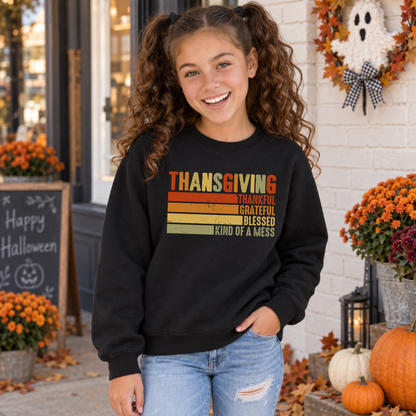 Girl wearing a black youth sweatshirt with retro Thanksgiving Thankful Grateful Blessed Kind of a Mess design near pumpkins.