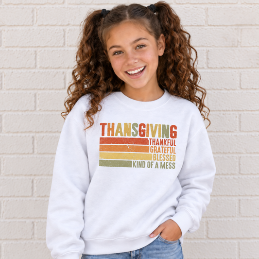Girl wearing a white youth sweatshirt with retro Thanksgiving Thankful Grateful Blessed Kind of a Mess design by a white brick wall.