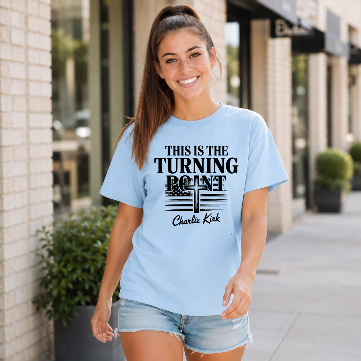 Woman wearing a light blue T-shirt with black This Is the Turning Point cross graphic.