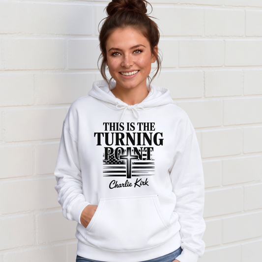 Woman wearing a white hoodie with black This Is the Turning Point lettering, a cross, and Charlie Kirk signature graphic.