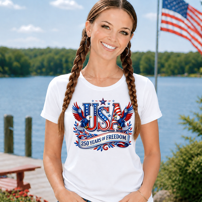 Woman wearing a white t-shirt with 'USA 250 Years of Freedom' design by a lake with an American flag in the background.