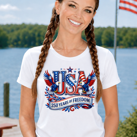 Woman wearing a white t-shirt with 'USA 250 Years of Freedom' design by a lake.