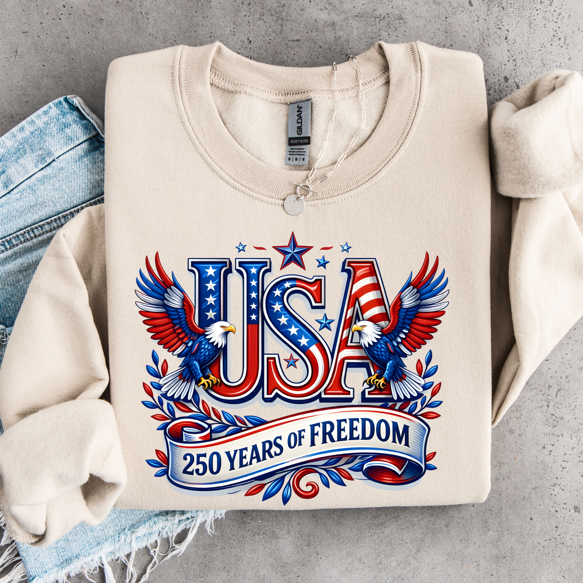 Beige sweatshirt with 'USA 250 Years of Freedom' design on a gray surface