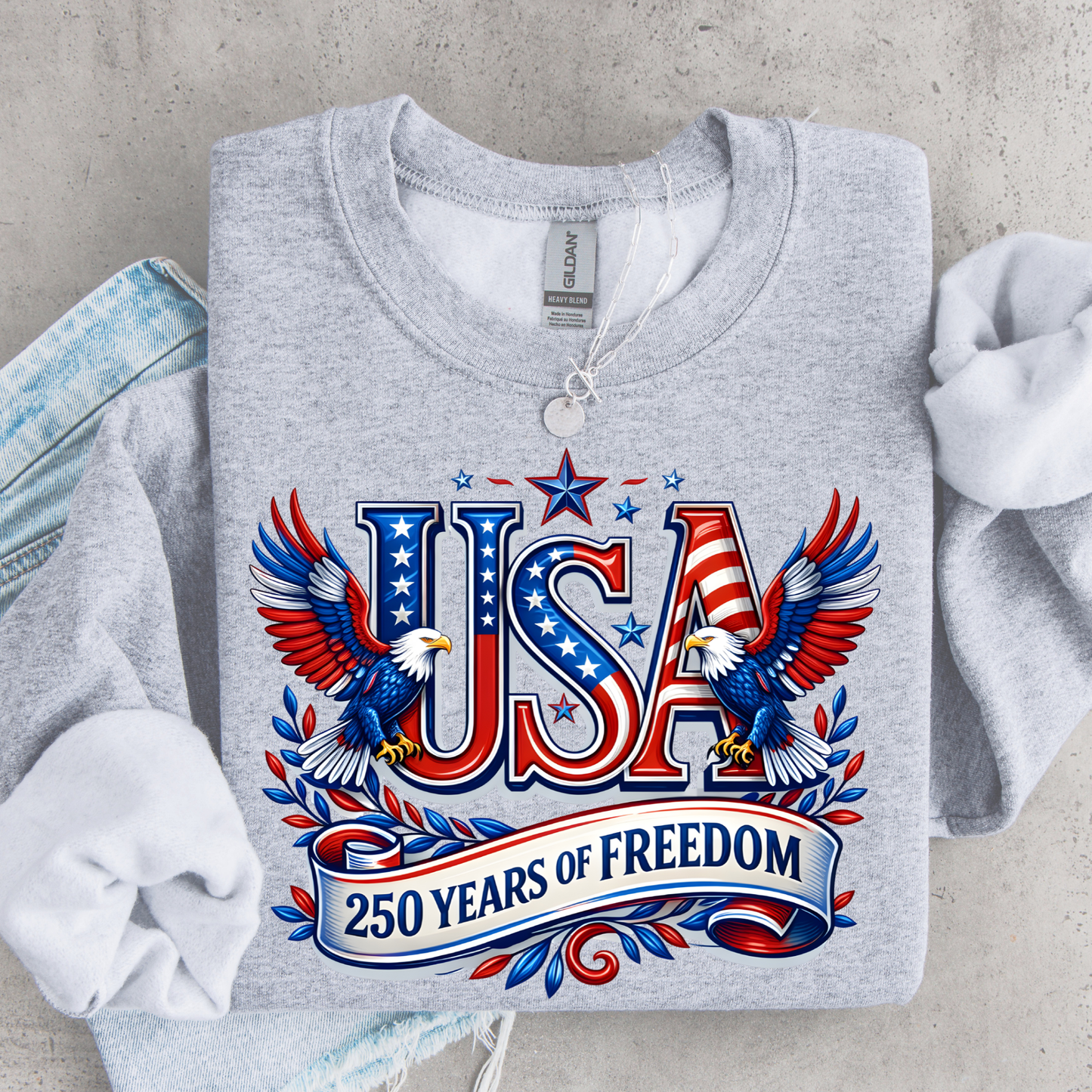 Gray sweatshirt with 'USA 250 Years of Freedom' design on a concrete surface