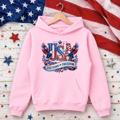 Pink hoodie with 'USA 250 Years of Freedom' design on a wooden surface with American flag and stars.