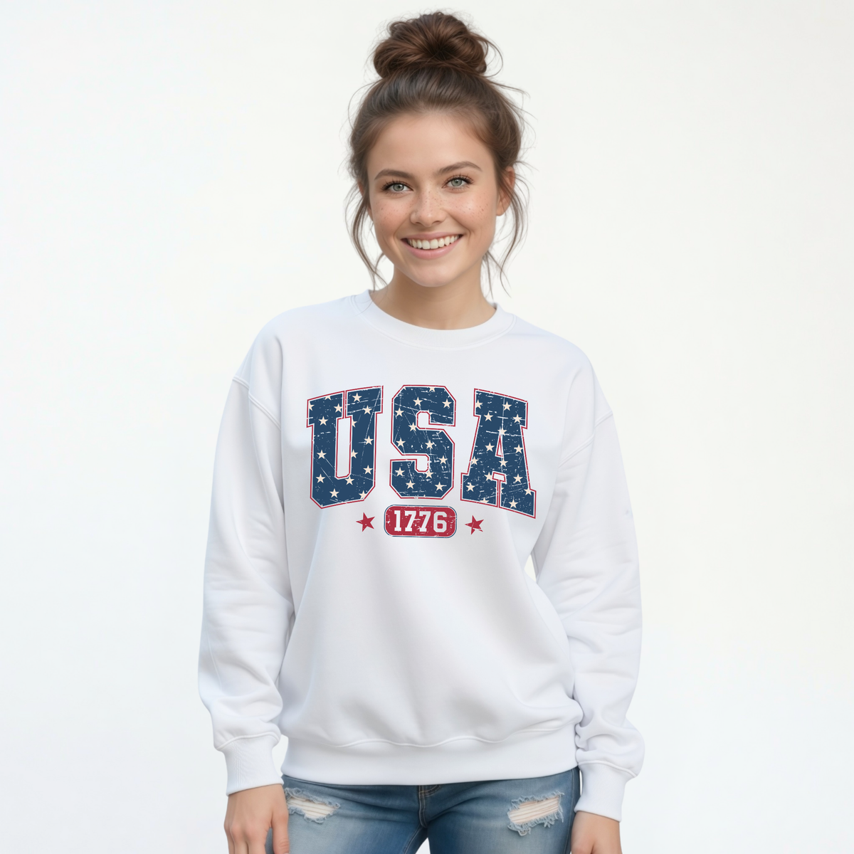 Smiling woman in a white crewneck sweatshirt with a navy USA graphic filled with white stars and red 1776 lettering