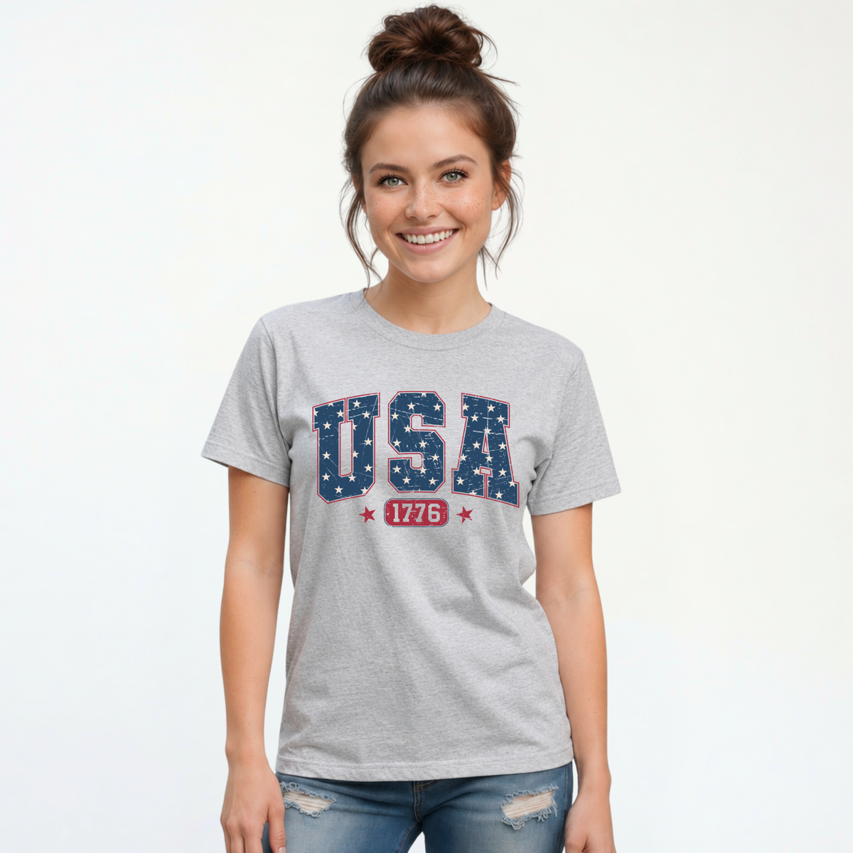 Smiling woman in a sports gray T-shirt with a navy USA graphic filled with white stars and red 1776 lettering