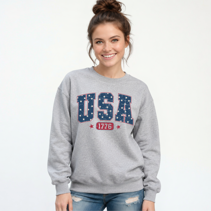 Smiling woman in a sports gray crewneck sweatshirt with a navy USA graphic filled with white stars and red 1776 lettering