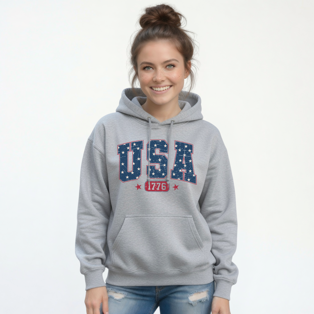 Smiling woman in a sports gray pullover hoodie with a navy USA graphic filled with white stars and red 1776 lettering
