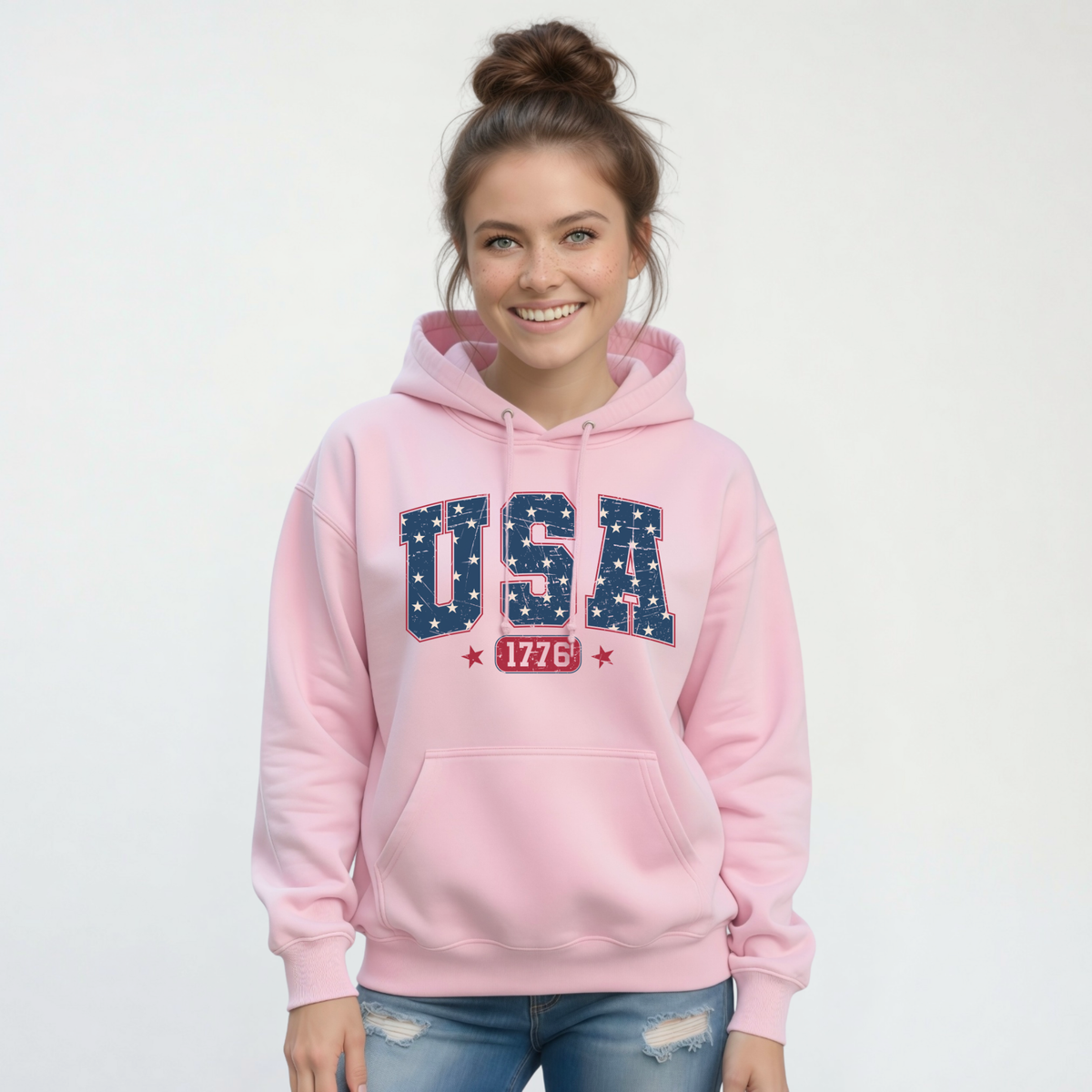 Smiling woman in a light pink pullover hoodie with a navy USA graphic filled with white stars and red 1776 lettering