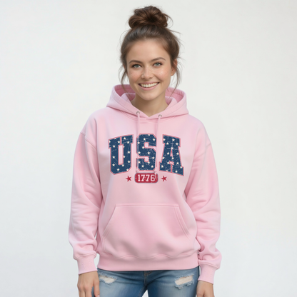 Smiling woman in a light pink pullover hoodie with a navy USA graphic filled with white stars and red 1776 lettering