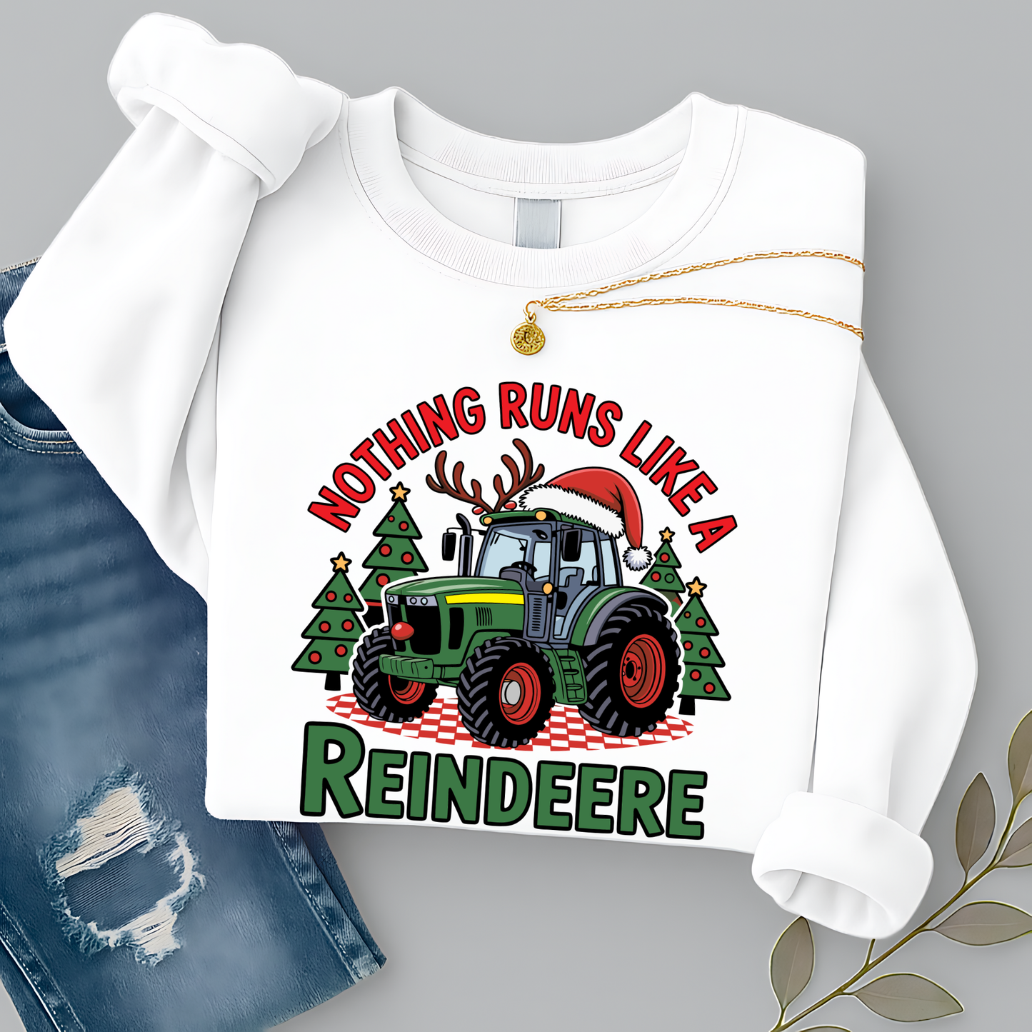 White sweatshirt with Christmas-themed design featuring a tractor and reindeer, paired with jeans on a gray background.