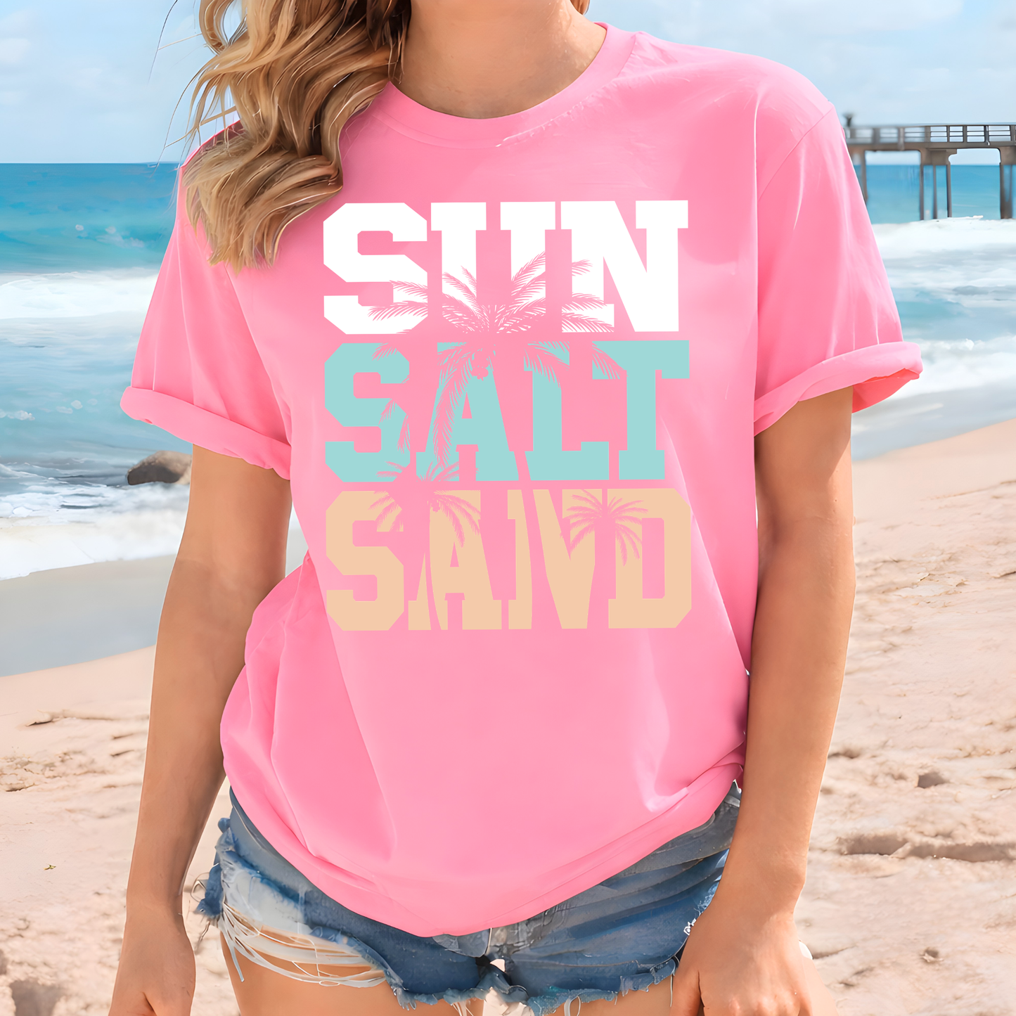 Woman wearing a pink t-shirt with 'Sun Salt Sand' text on a beach