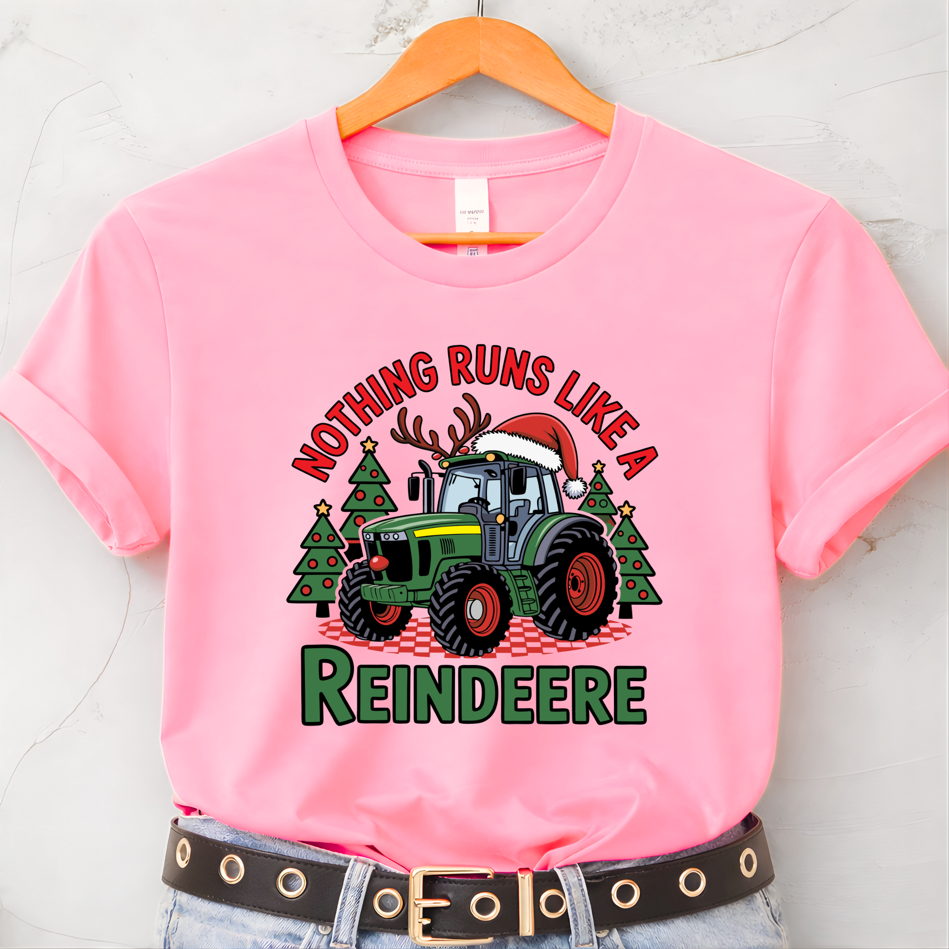 Pink t-shirt with Christmas tractor graphic and text on a hanger