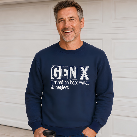 Man wearing a navy Gen X crewneck sweatshirt with distressed “Raised on hose water & neglect” lettering in front of a garage.