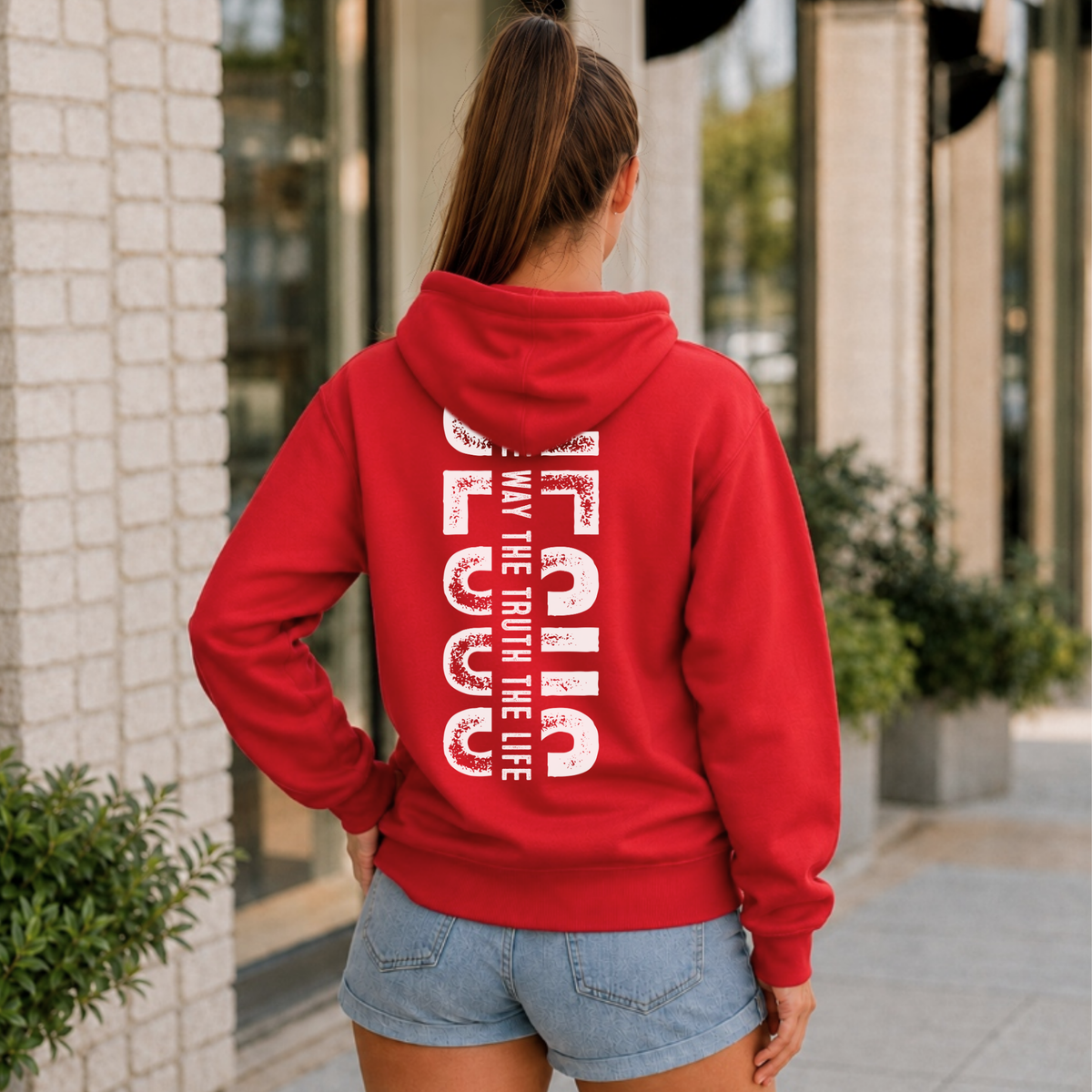 Woman shown from behind wearing a red hoodie with vertical white JESUS lettering and “The Way, The Truth, The Life” text.
