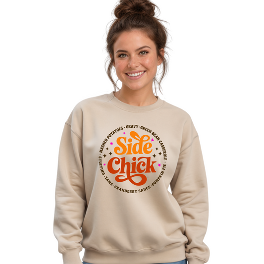 A woman wearing a beige crewneck sweatshirt with a colorful Thanksgiving 'Side Chick' graphic, posing against a white brick wall.