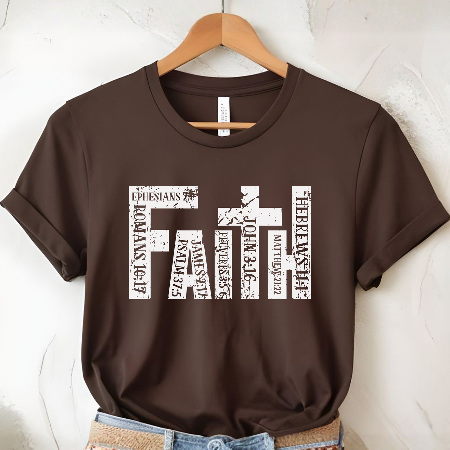 Brown t-shirt with 'FAITH' design on a hanger against a white wall.