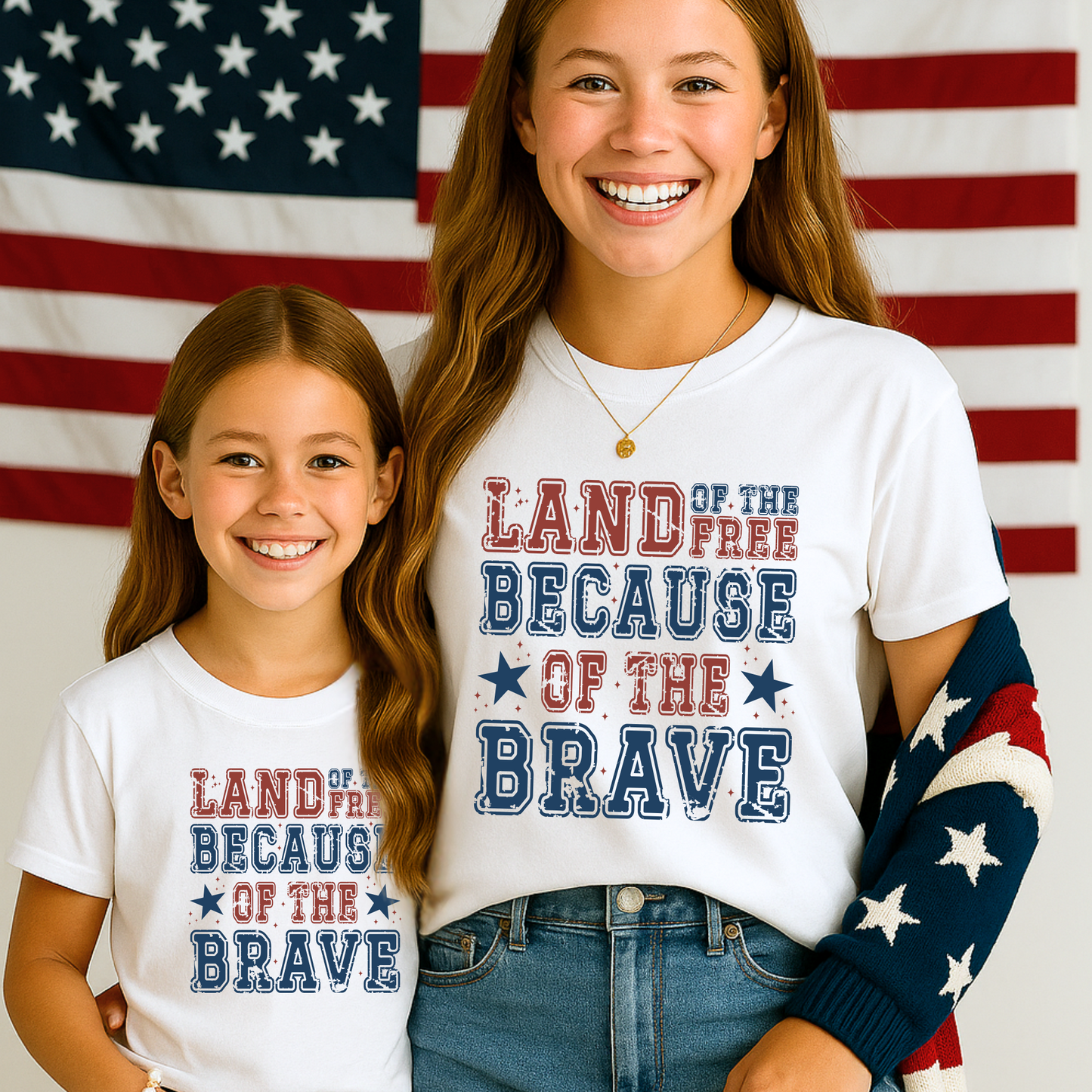 Young girls wearing white "Land of the Free Because of the Brave" t-shirt with American Flag in the background 