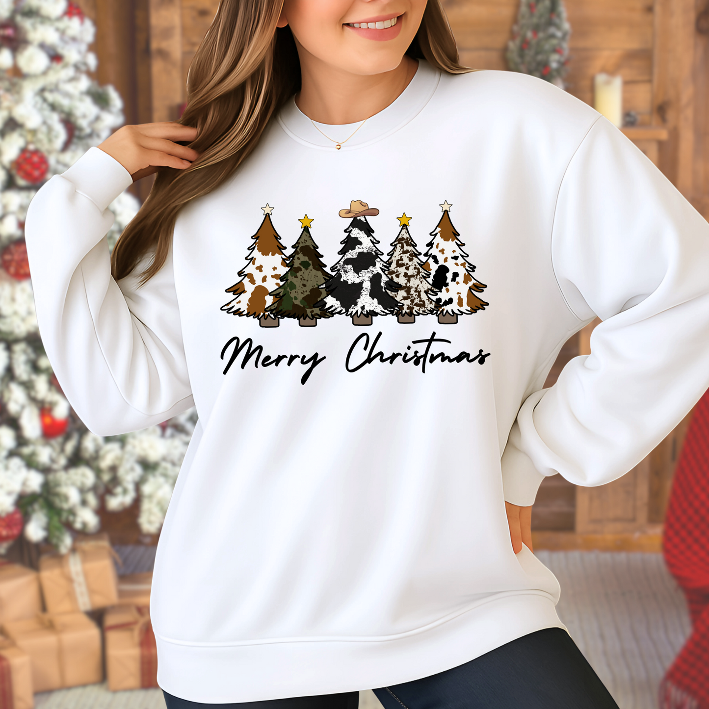 Lady wearing a white sweatshirt with Christmas tree and cow design, standing in front of a decorated Christmas tree.