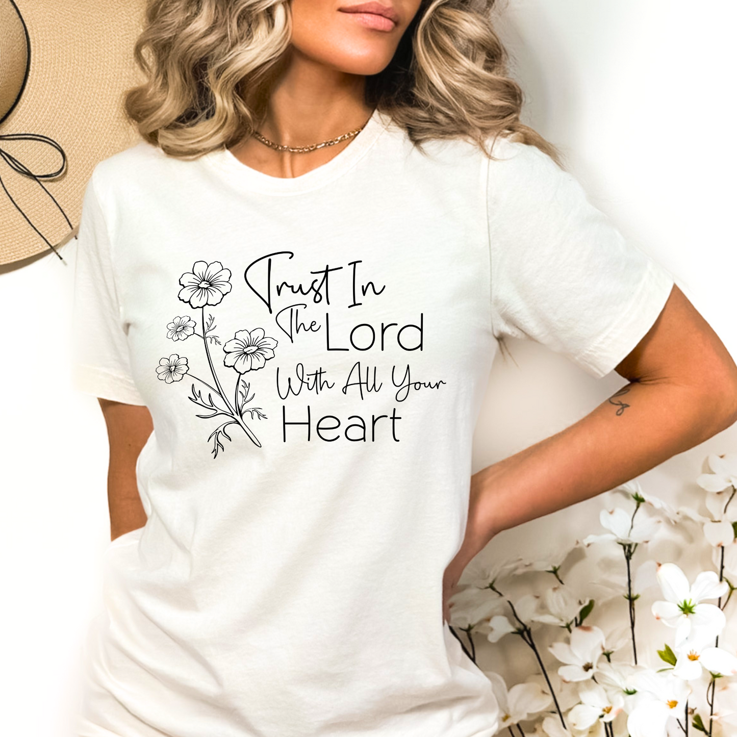 Woman wearing white T-shirt with floral graphic and “Trust in the Lord With All Your Heart” text.