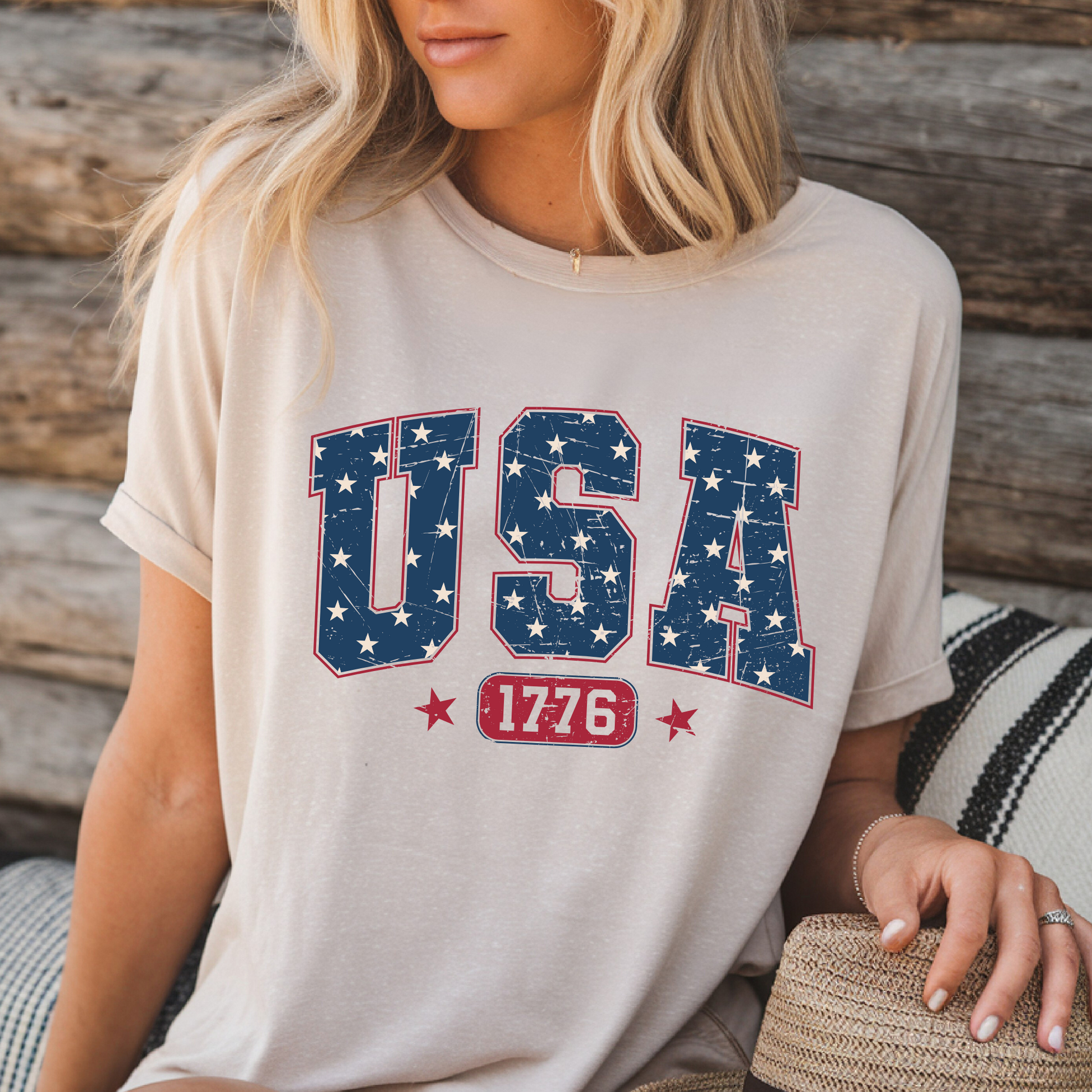 USA 1776 graphic T-shirt in sand color, patriotic tee styled for summer by woman sitting on wooden bench