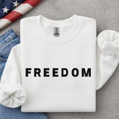 White sweatshirt with 'FREEDOM' text on a gray surface with jeans and an American flag.