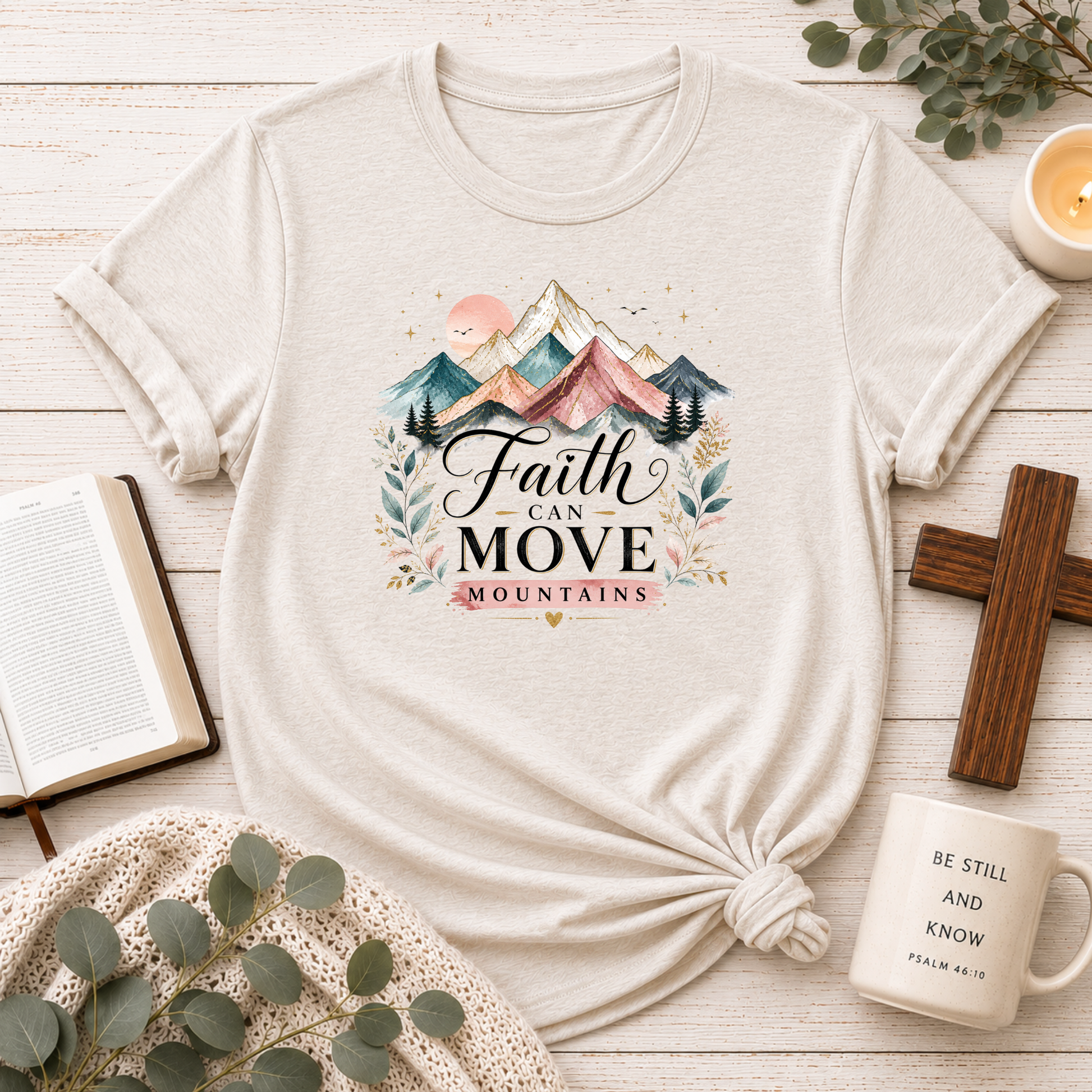 White t-shirt with 'Faith can move mountains' design on a wooden surface with decor items.