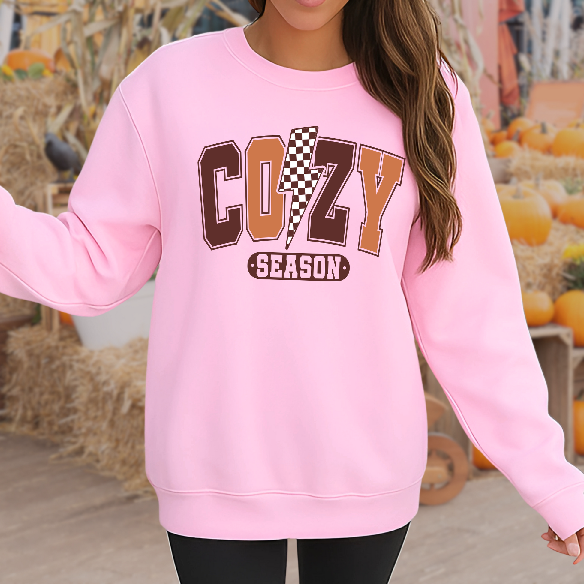 Woman in light pink Cozy Season sweatshirt standing in a fall pumpkin patch