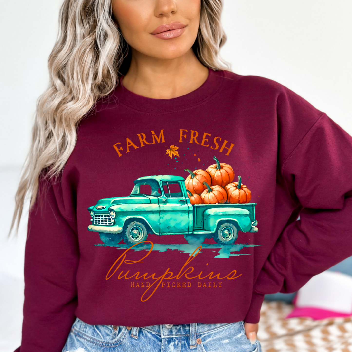 Woman in maroon pumpkin truck sweatshirt styled with ripped jeans for fall