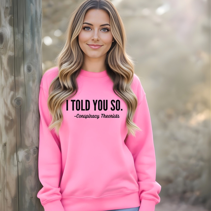 Woman wearing a bright pink sweatshirt with text 'I Told You So. - Conspiracy Theorists' outdoors.