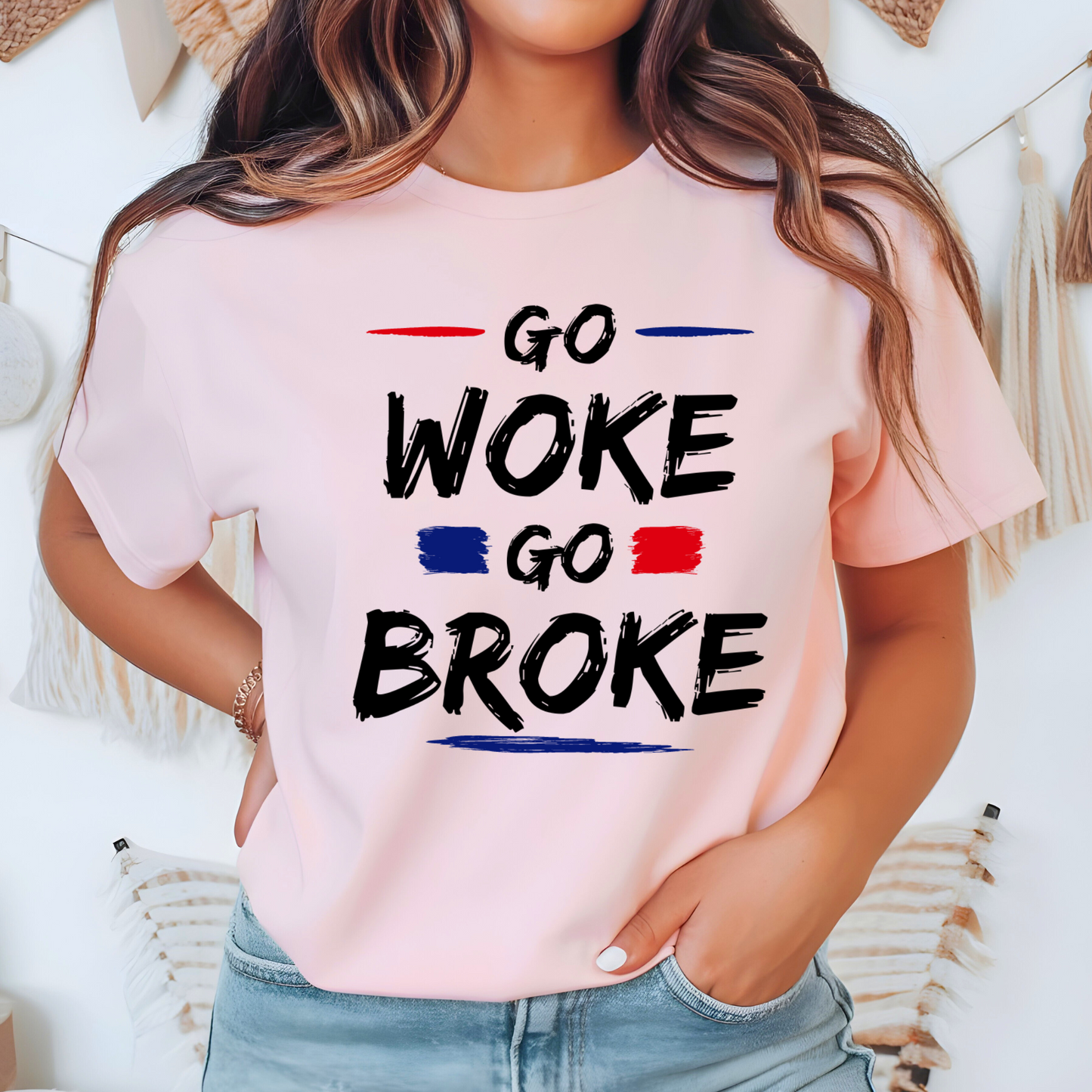 Woman wearing a light pink “Go Woke Go Broke” t-shirt with bold black, red, and blue lettering
