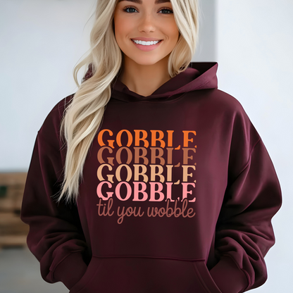 Woman wearing a maroon hoodie with “Gobble Til You Wobble” Thanksgiving design – cozy fall fashion