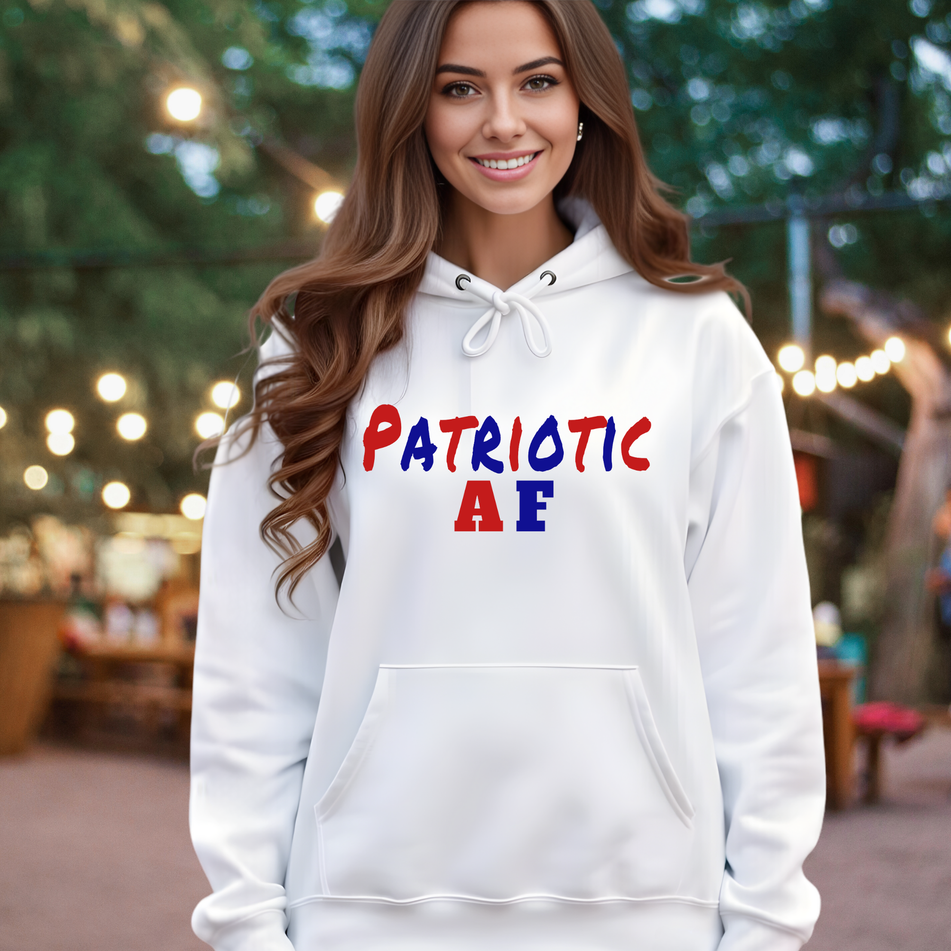 Woman wearing a white hoodie with 'Patriotic AF' text, standing outdoors with blurred lights and trees in the background.