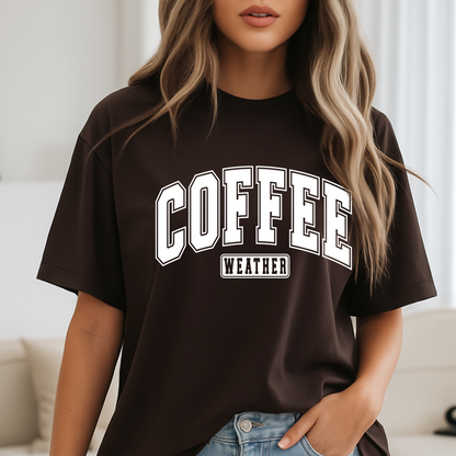 Woman wearing brown "Coffee Weather" shirt standing by bed, cozy fall look