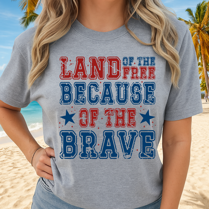 Woman wearing gray t-shirt with “Land of the Free Because of the Brave” design, standing on the beach

