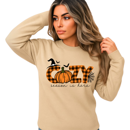 Woman wearing light sand sweatshirt with “Cozy Season Is Here” design – pumpkin, plaid, bats, spiderweb