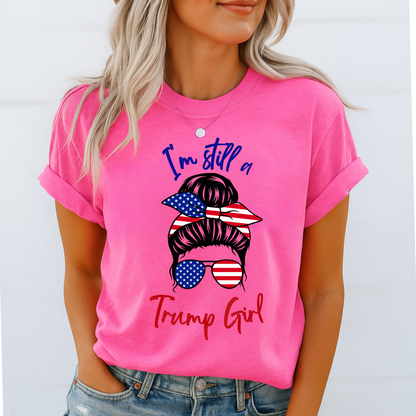 Woman wearing pink “I’m Still a Trump Girl” patriotic T-shirt with USA flag bun and sunglasses design.