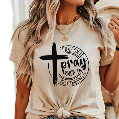 Woman wearing tan T-shirt with black cross graphic and inspirational pray wording.