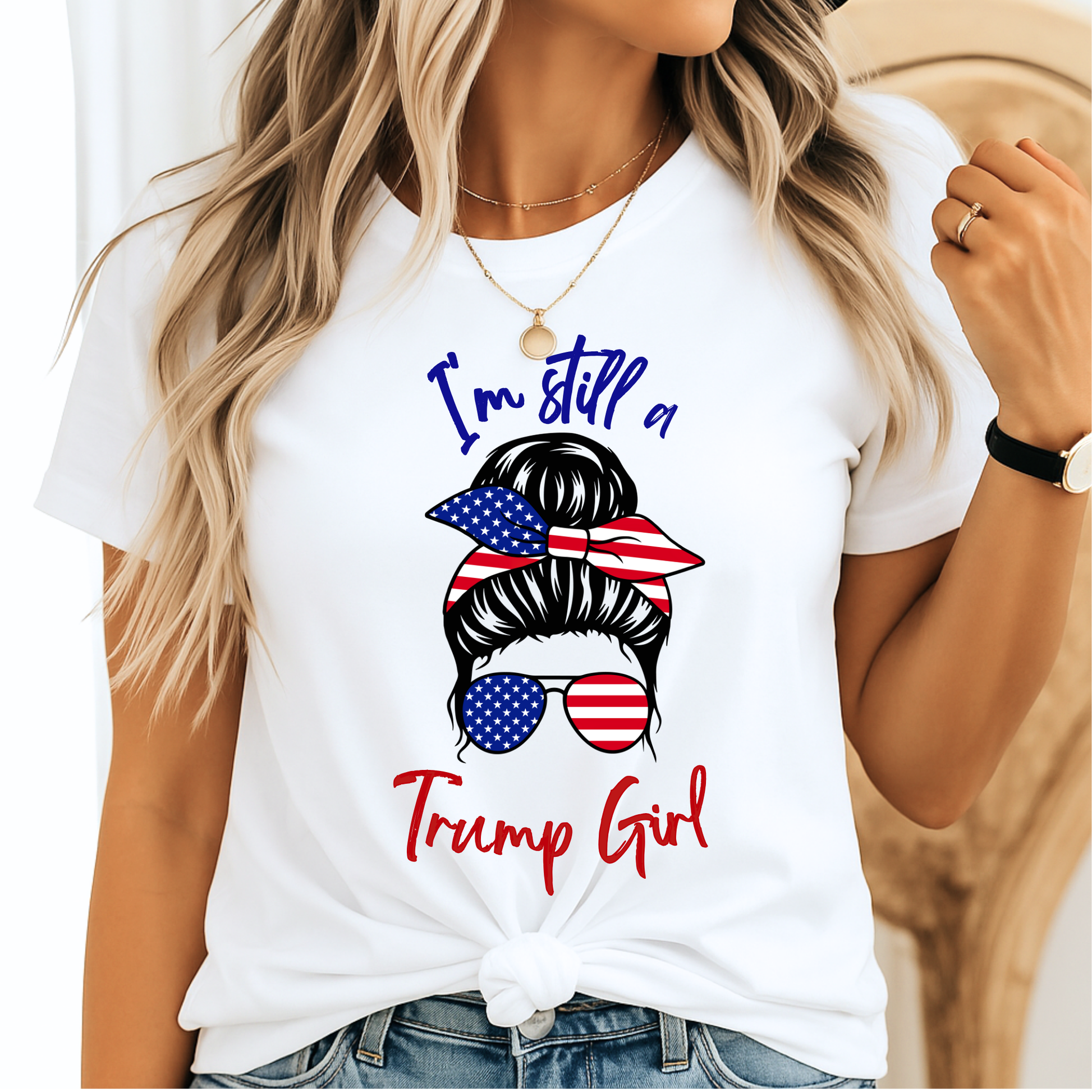 Woman wearing white “I’m Still a Trump Girl” patriotic T-shirt with USA flag bun and sunglasses design.