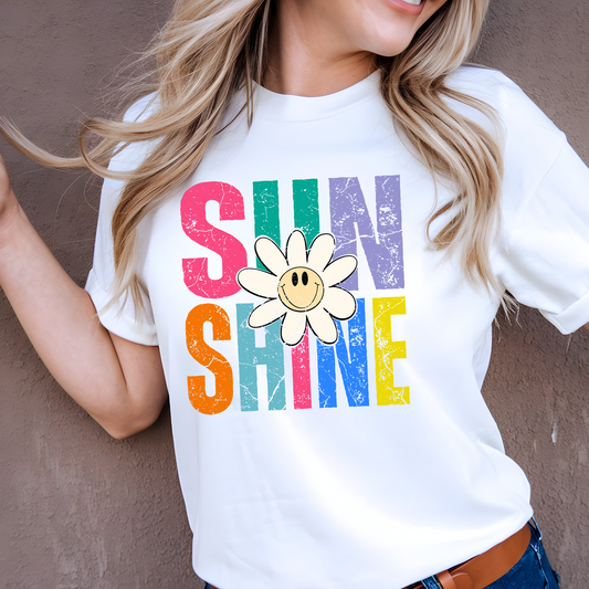 Woman wearing white shirt with rainbow “SUNSHINE” and smiley daisy
